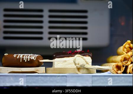 Close-up view of a pyramid stack of sweet, crispy golden waffle rolls filled with boiled condensed milk, displayed on a shelf in a pastry shop or cafe display case. Stock Photo