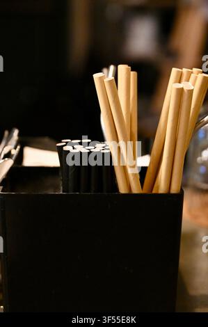 Close-up view of drinking straws in beige and black colors standing in a black organizer box on a restaurant or cafe bar counter. Stock Photo