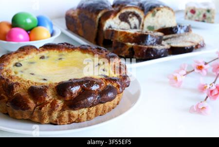 Traditional Romanian Easter cake Pasca with sweet cheese and raisin, next to colored eggs, spring flowers and Cozonac sweet bread on white table. Stock Photo