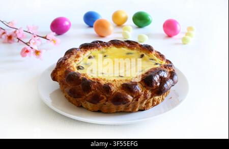 Traditional Romanian Easter cake Pasca with sweet cheese and raisin, next to colored eggs and spring flowers on white table. Easter and holiday season. Stock Photo