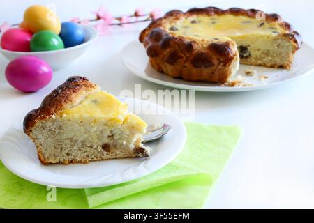 Slice of traditional Romanian Easter Pasca cake with cottage cheese and raisins, next to colored eggs on white table. Easter and holiday concept. Stock Photo