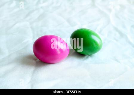 Two Easter eggs dyed in vibrant pink and green, placed on a soft light sage green cloth background. Modern minimalist concept. Stock Photo