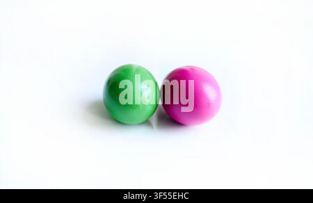 Two vibrant green and magenta colored Easter eggs side by side isolated on a clean white surface with subtle reflections. Modern minimalist concept. Stock Photo