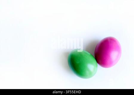 Two vibrant green and magenta colored Easter eggs side by side isolated on a clean white surface with subtle reflections. Modern minimalist concept. Stock Photo
