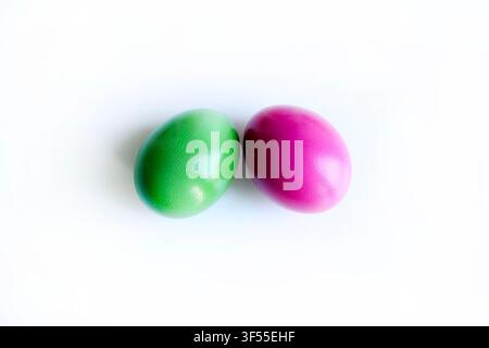 Two vibrant green and magenta colored Easter eggs side by side isolated on a clean white surface with subtle reflections. Modern minimalist concept. Stock Photo