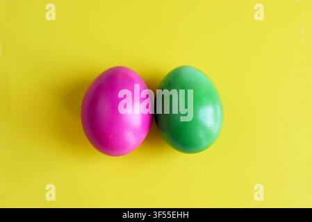 Two vibrant green and magenta colored Easter eggs side by side isolated on a clean yellow surface with subtle reflections. Modern minimalist concept. Stock Photo