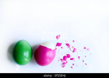 Whole green egg and peeled fuchsia egg with shell fragments on white background. Easter and rebirth concept. Stock Photo