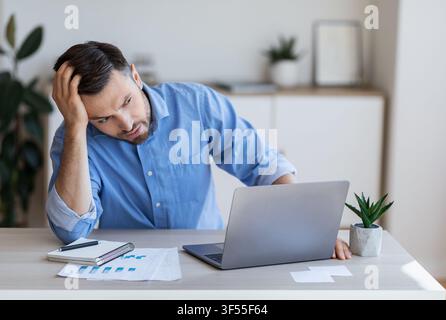 Stressed tired businessman having problems at work, sitting at desk with laptop Stock Photo