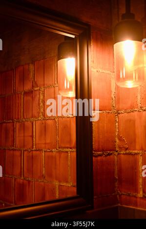 Close-up indoor view of a modern bathroom or hallway interior featuring a dark-framed mirror reflecting a ceramic block wall, illuminated by a warm pendant light. Stock Photo
