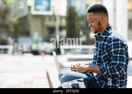 Glad black man using laptop, side view Stock Photo