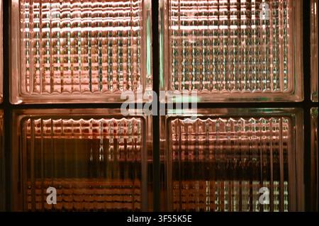 Close-up view of textured glass blocks forming a translucent window wall, illuminated from behind with warm glowing light creating a geometric pattern. Stock Photo