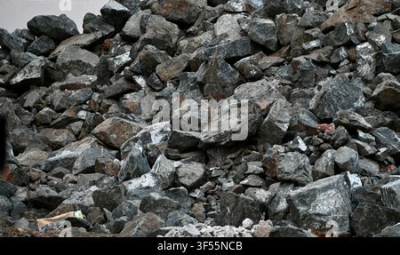 Close-up view of a large pile of dark grey and black crushed stone, gravel, and rock aggregate for construction and industrial use. Stock Photo