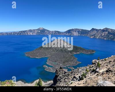 Wizard Island is surrounded by the deep blue water of Crater Lake in Crater Lake National Park, Oregon, USA. Stock Photo