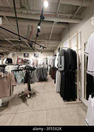 Pforzheim, Germany July 30, 2026 Modern clothing shop aisle shows shirts and jackets hanging on metal racks under bright ceiling spotlights, with pric Stock Photo