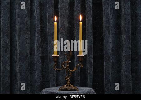 Two burning yellow candles on an ornate vintage brass candlestick against a dark textured background. Stock Photo