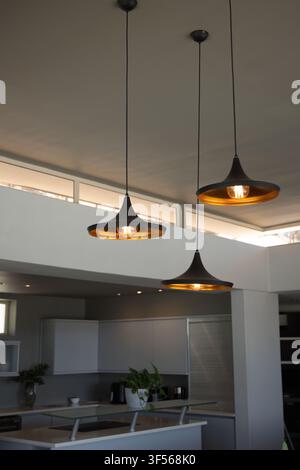 Three black pendant lamps are glowing over kitchen island with cooktop and potted plant Stock Photo