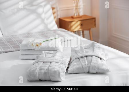Clean bathrobes with flowers and towels on bed indoors, closeup Stock Photo