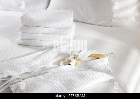 Clean bathrobe, towels and flowers on bed indoors, closeup Stock Photo