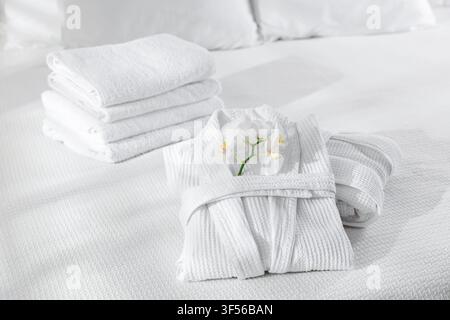 Clean bathrobes, towels and flowers on bed indoors, closeup Stock Photo