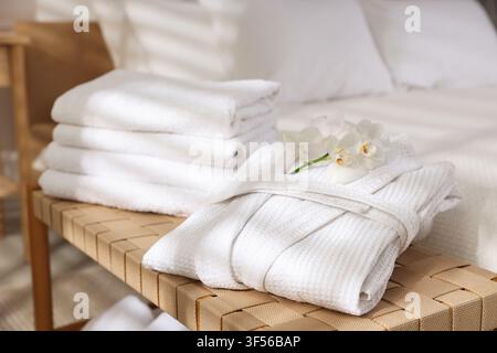 Clean bathrobe, towels and flowers on shelf of bed indoors, closeup Stock Photo