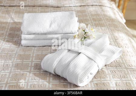 Clean bathrobe, towels and flowers on bed indoors, closeup Stock Photo