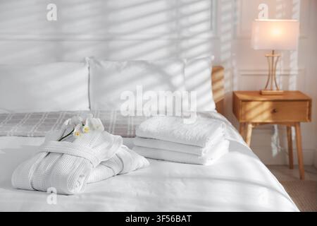 Clean bathrobes with flowers and towels on bed indoors Stock Photo