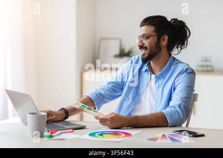 Graphic Design Courses Online. Arab Man Holding Colour Swatch And Using Laptop Stock Photo