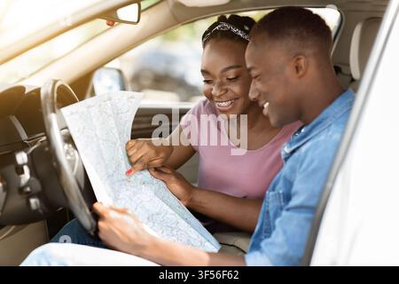 Enthusiastic black couple reading map while having car trip Stock Photo