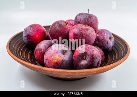 Fresh Ripe Red Plums Arranged in Rustic Ceramic Bowl on White Background Stock Photo