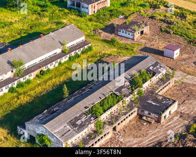 Aerial view of abandoned industrial buildings with damaged roofs and overgrown vegetation surrounded by rural fields in Lublewo Leborskie, Wojewodztwo Stock Photo