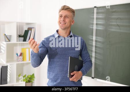 Smiling teacher with laptop near chalkboard in classroom Stock Photo