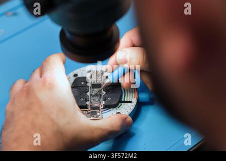 Technician repairs electronic circuit board with precision tools under magnifying lamp in a workshop setting Stock Photo
