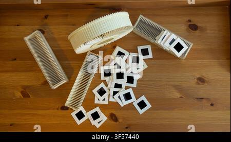 Several slide holders and scattered 35mm film slides on a wooden surface. Film slides are square with black frames. Slide holders are beige plastic, s Stock Photo