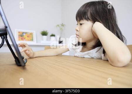 Japanese girl using a tablet PC in dining room (7 years old) Stock Photo