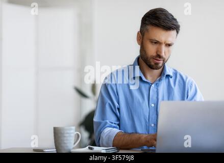 Concentrated businessman working on laptop at workplace in office, typing on keyboard Stock Photo