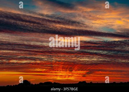 Layered red and orange clouds glowing intensely above a dark horizon at sunset Stock Photo