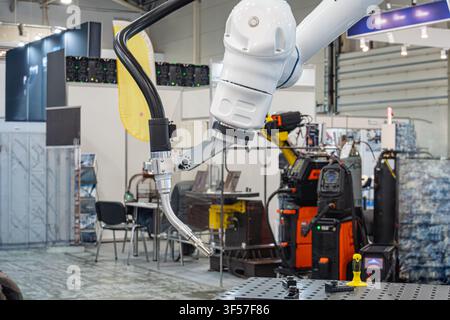 Robotic arm in industrial setting at exhibition, showcasing automation technology, metallic structure, welding machine, clean layout, bright even ligh Stock Photo