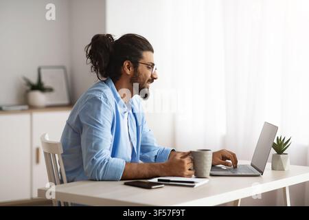 Remote Work. Male Freelancer Using Laptop And Drinking Coffee At Home Office Stock Photo
