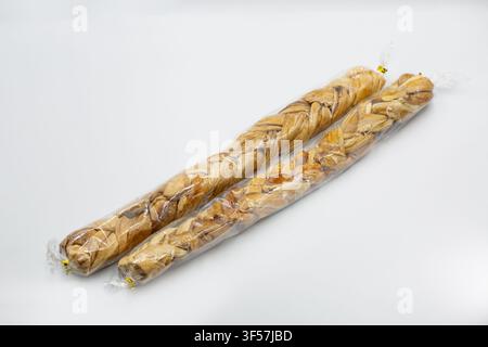 Studio shot of braided dried melon snacks wrapped in clear plastic. Natural sweet fruit product closeup on white, highlighting texture and packaging. Stock Photo