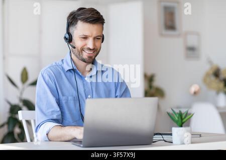Call center operator at work. Male manager wearing headset and using laptop Stock Photo