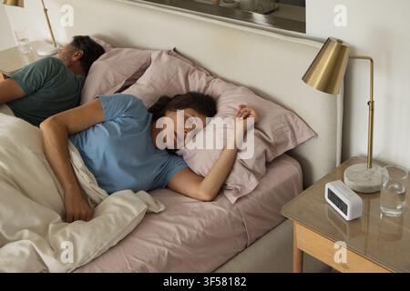 Mature couple sleeping on bed in bedroom with pale pink sheets, cream duvet, brass lamp Stock Photo