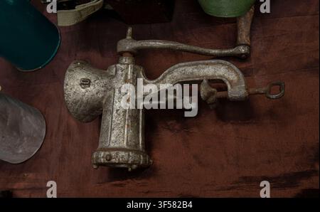 A manual metal meat grinder sits on dark fabric. This kitchen tool shows a design from a past era. It has a hand crank for grinding meat. Stock Photo