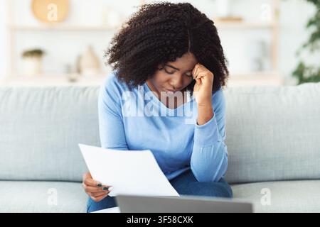 Sad black woman holding papers sitting with laptop Stock Photo