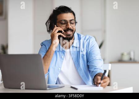 Young Arab Male Entrepreneur Talking On Cellphone And Taking Notes In Office Stock Photo