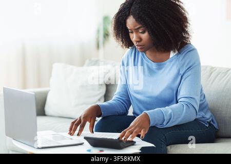 Woman using calculator and laptop at home Stock Photo