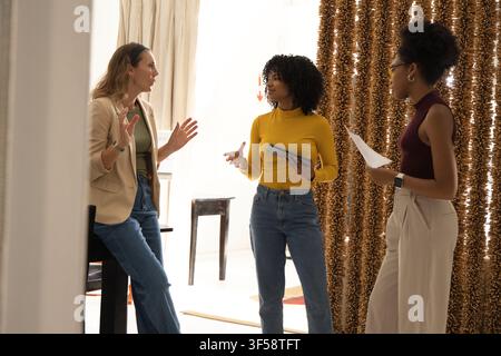 Diverse female colleagues standing and discussing project in studio with tablet paper beige blazer Stock Photo