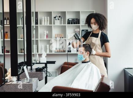 Hairdresser drying hair of male client, both observing safety measures Stock Photo