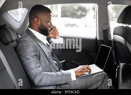 Young black businessman using mobile phone and laptop in car Stock Photo