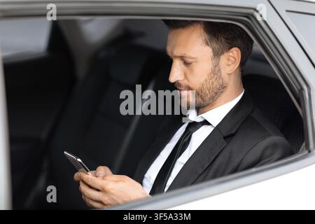 Wealthy manager sitting in car and using smartphone Stock Photo