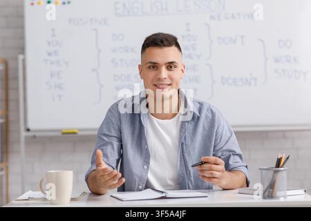 Online teacher speaking by webcam, sitting at table in home office and explaining rules english grammar Stock Photo